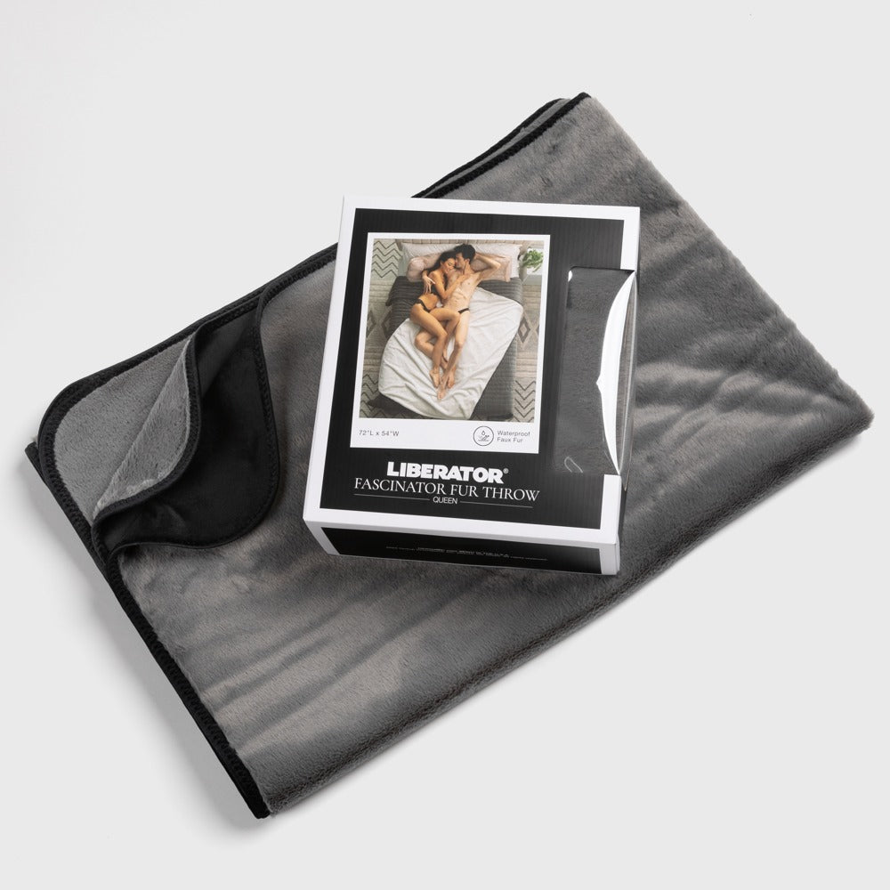 Liberator Faux-Fur Fascinator – quadratisch gefaltete graue Liebesdecke mit schwarzer Kunstfellseite und mittig platzierter Originalverpackung mit Liberator Markenlogo in schräger Draufsicht auf weißem Hintergrund – erhältlich bei Evoria Care