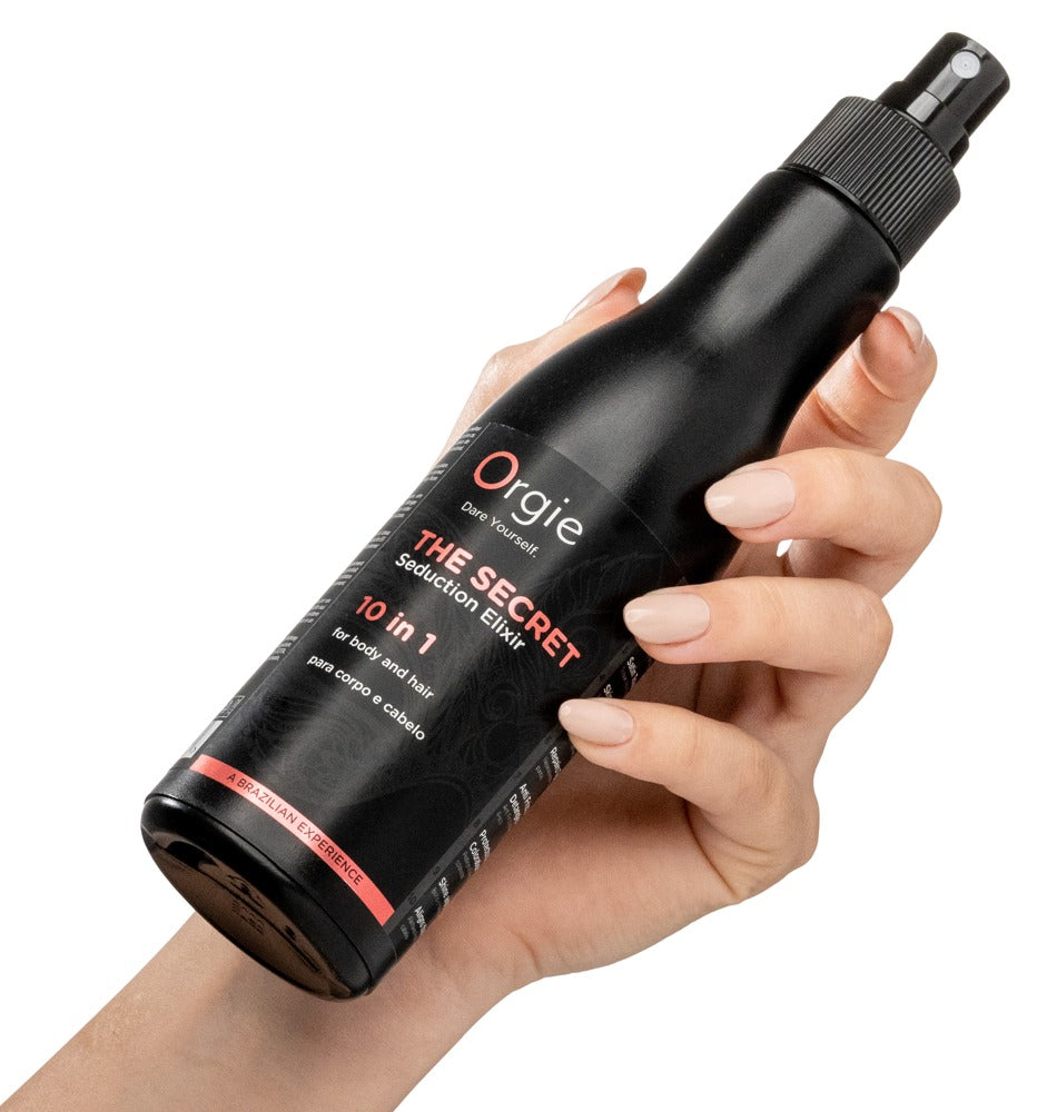 Orgie Secret Seduction Elixir Körper- und Haarlotion in schwarzer Sprühflasche mit roter Beschriftung, schräg in einer Hand gehalten zur Veranschaulichung von Größe, Sprühkopf und Handhabung – erhältlich bei Evoria Care