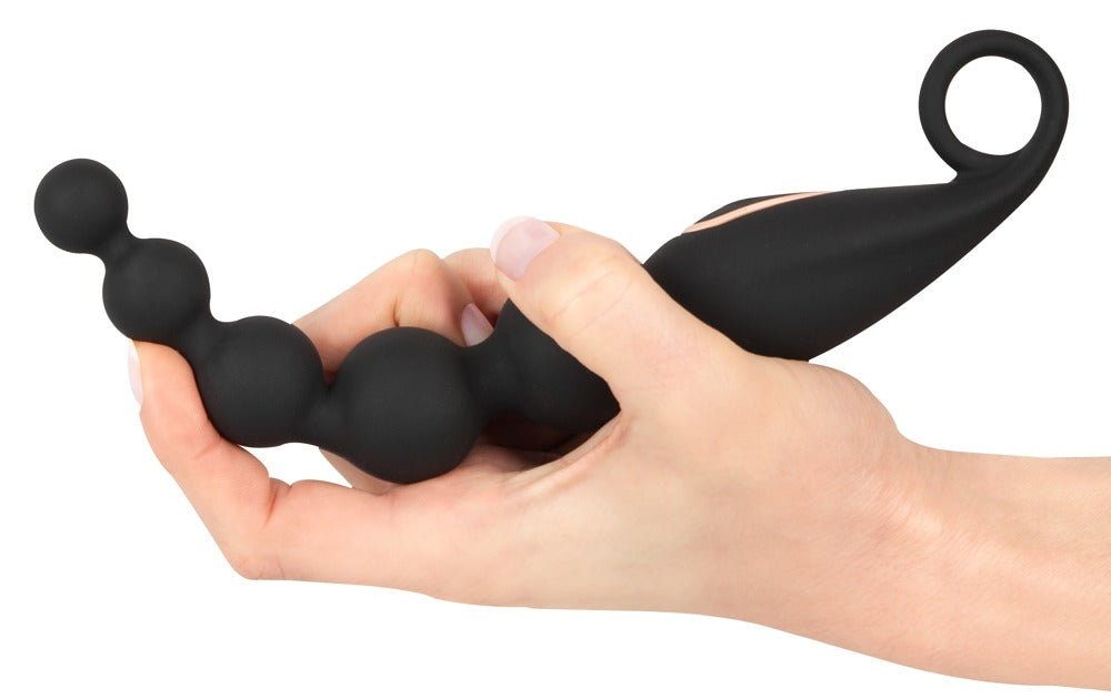 ANOS vibrierende Analperlen in Schwarz – Größenvergleich in einer Hand mit sichtbarem flexiblem Kugeldesign und Ringgriff