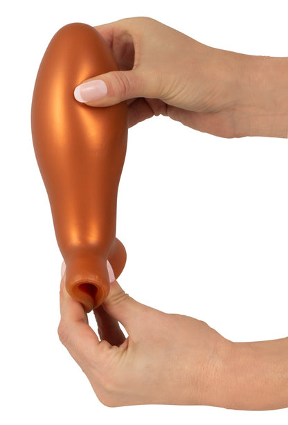 ANOS XL Analplug aus Liquid Silicone – Darstellung der flexiblen orangefarbenen Form zwischen zwei Händen