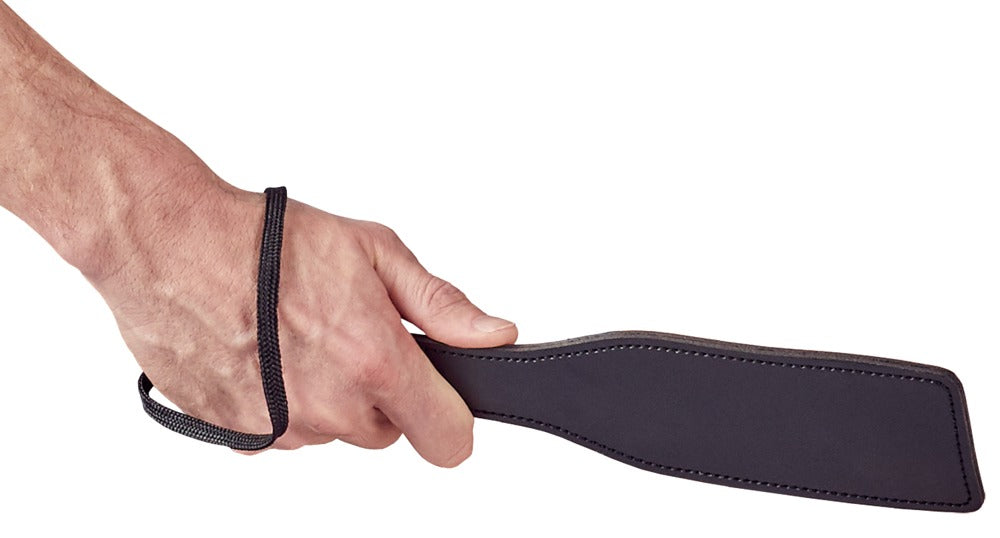 Bad Kitty BDSM Starter-Set schwarze Schlaggerte mit flacher breiter Schlagfläche und schlankem Griff, in einer Hand gehalten in seitlicher Detailansicht – erhältlich bei Evoria Care
