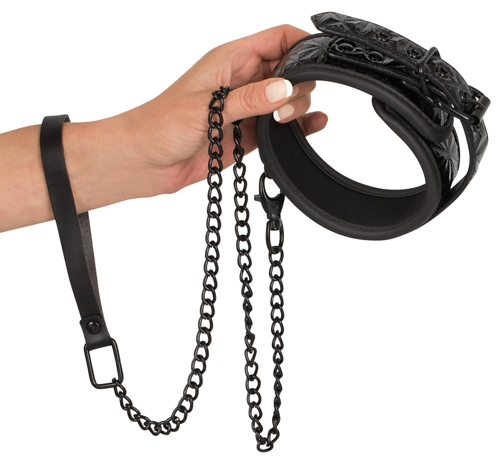Bad Kitty gepolsterte Halsfessel in Schwarz mit silberfarbener Kettenleine, Metallringen und Befestigungselementen, von einer Hand gehalten in detaillierter Produktansicht – erhältlich bei Evoria Care