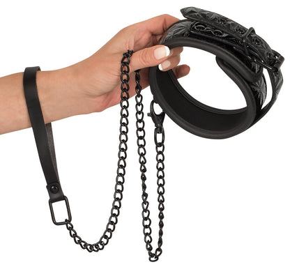 Bad Kitty gepolsterte Halsfessel in Schwarz mit silberfarbener Kettenleine, Metallringen und Befestigungselementen, von einer Hand gehalten in detaillierter Produktansicht – erhältlich bei Evoria Care