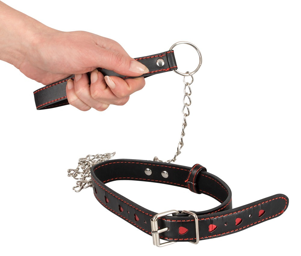 Bad Kitty Halsfessel und Leine in schwarzer Leder-Optik mit silberfarbener Kettenleine, Metallverschlüssen und dekorativen Herzdetails, von einer Hand gehalten in detaillierter Produktansicht – erhältlich bei Evoria Care
