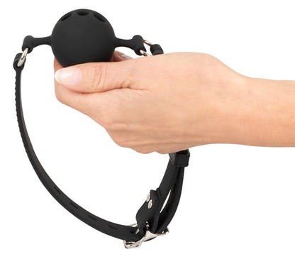 Bad Kitty Silikon-Ballknebel mit schwarzem rundem Mundstück, integrierten Atemöffnungen und verstellbarem Kopfriemen, von einer Hand gehalten zur Veranschaulichung der Form und Handhabung – erhältlich bei Evoria Care