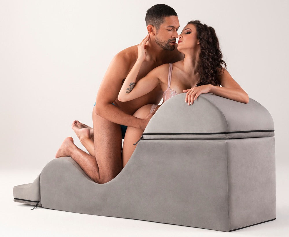 Liberator Aria Flip Chaise – graue Premium-Sexlounge in kompakter Position, auf der eine erwachsene Frau in schwarzer Kleidung mit angewinkelten Beinen sitzt und die erhöhte Sitzfläche demonstriert – erhältlich bei Evoria Care