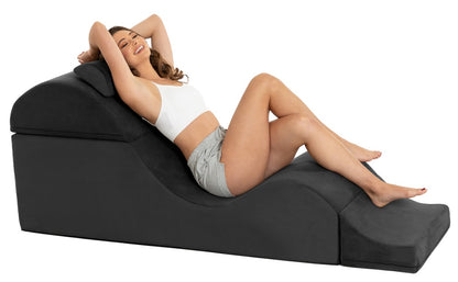 Liberator Aria Flip Chaise – schwarze Premium-Sexlounge mit geschwungener Polsterform, auf der eine erwachsene Frau mit erhöht gelagertem Oberkörper und angewinkelten Beinen liegt – erhältlich bei Evoria Care