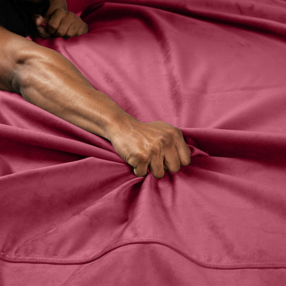 Liberator Fascinator Throw – bordeauxrote Premium-Liebesdecke mit weicher Textiloberfläche, ausgebreitet auf einem Bett mit sichtbarer Hand einer erwachsenen Person auf dem Stoff – erhältlich bei Evoria Care