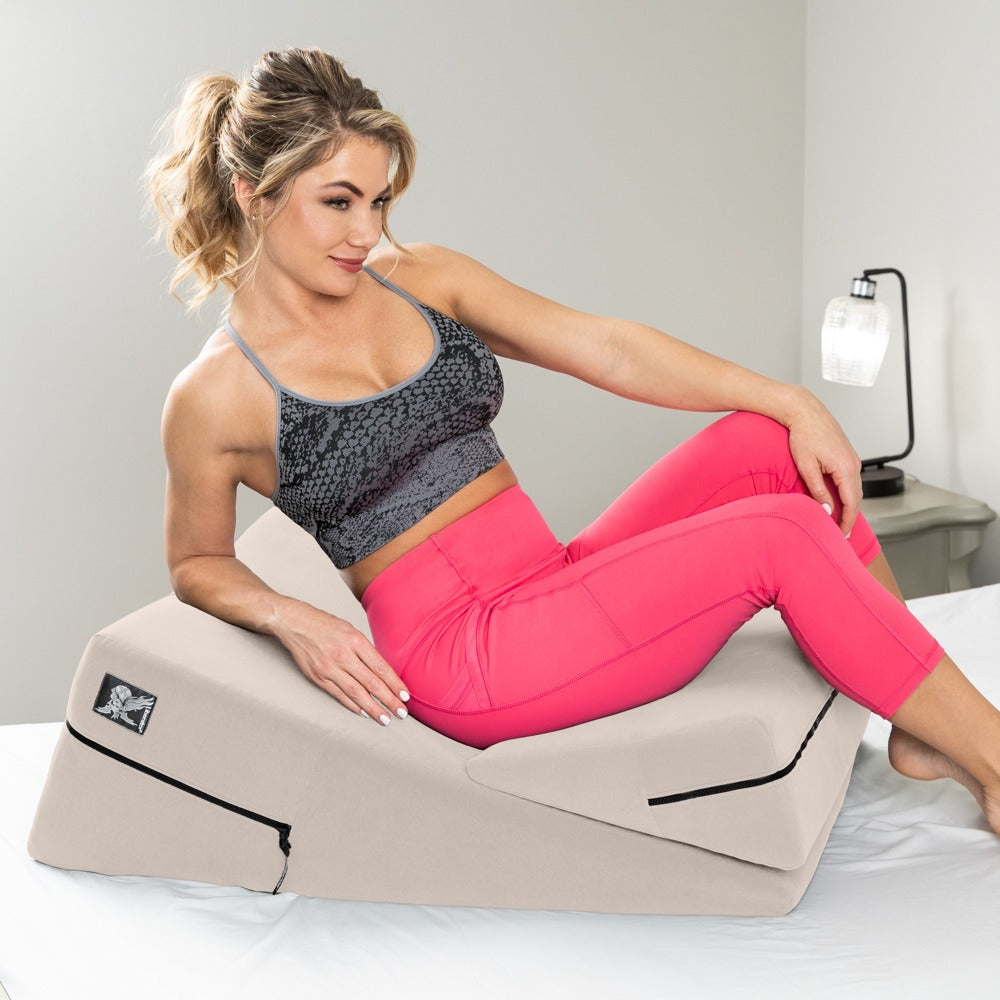 Liberator Wedge/Ramp Combo – beigefarbenes Positionierungsset auf einem hellen Bett, demonstriert von einer erwachsenen Frau in grauem Oberteil und pinkfarbener Hose in sitzender Position auf den gestapelten Kissen – erhältlich bei Evoria Care