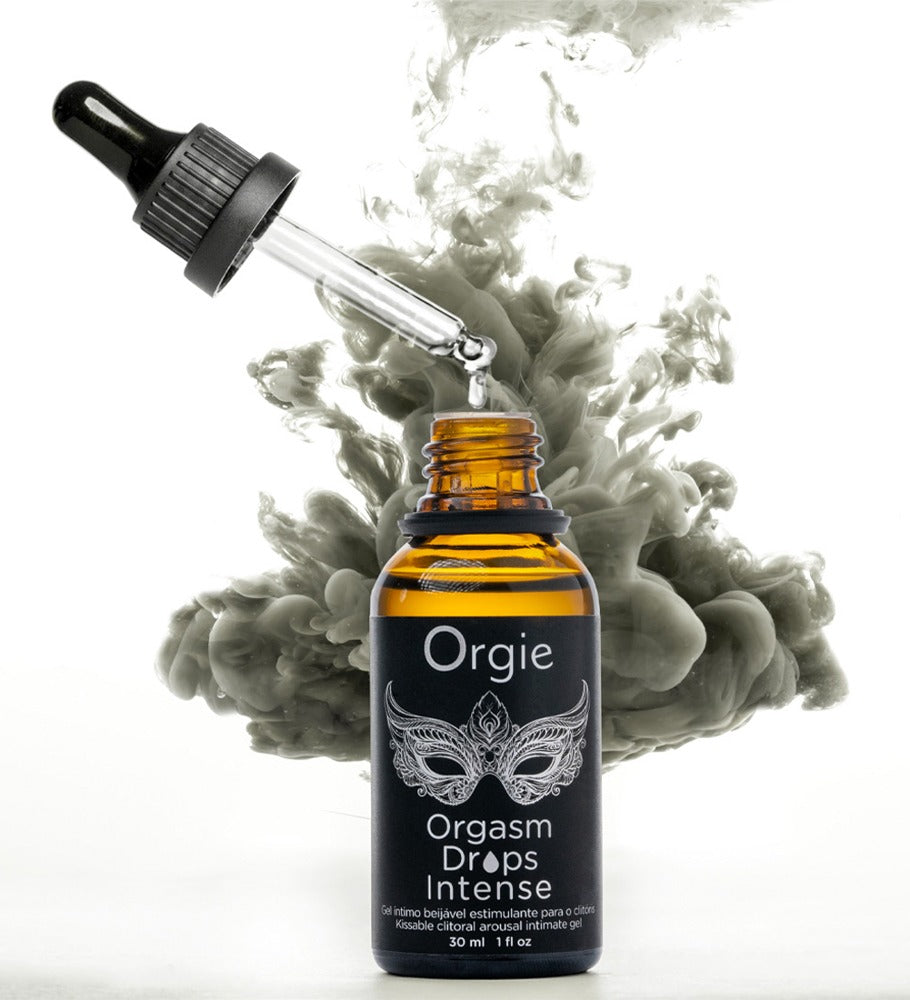 Orgie Orgasm Drops Intense Klitoristropfen in schwarzer Pipettenflasche mit goldfarbenen Akzenten, dekorativ inszeniert zwischen weißen Blüten und grünen Pflanzen – erhältlich bei Evoria Care
