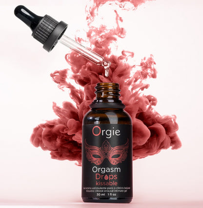 Orgie Orgasm Drops Kissable Klitoristropfen in schwarzer Pipettenflasche mit rotem Etikett, dekorativ inszeniert mit rosafarbenen und roten Blüten auf hellem Hintergrund – erhältlich bei Evoria Care