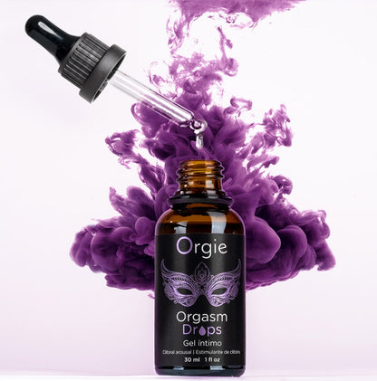 Orgie Orgasm Drops Klitoris-Tropfen in schwarzer Pipettenflasche mit violettem Etikett, dekorativ inszeniert mit violetten Blüten auf hellem Hintergrund – erhältlich bei Evoria Care
