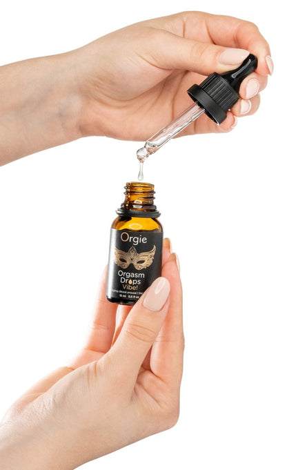 Orgie Orgasm Drops Vibe! Klitoristropfen in schwarzer Flasche mit herausgezogener Pipette, zwischen zwei Händen zur Veranschaulichung der Dosierung dargestellt – erhältlich bei Evoria Care