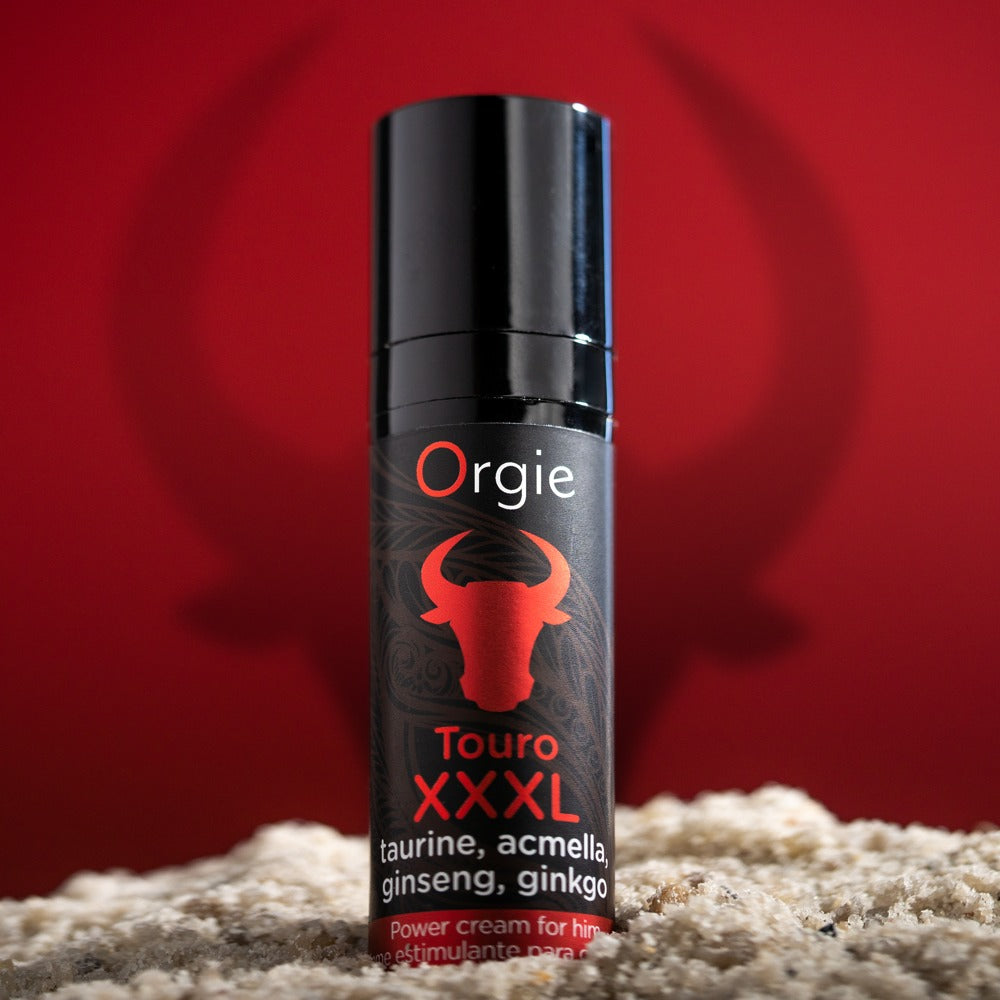 Orgie Touro XXXL Power Cream für Männer in schwarzer Flasche mit rotem Stiermotiv, dekorativ inszeniert auf hellem Untergrund vor kräftig rotem Hintergrund – erhältlich bei Evoria Care