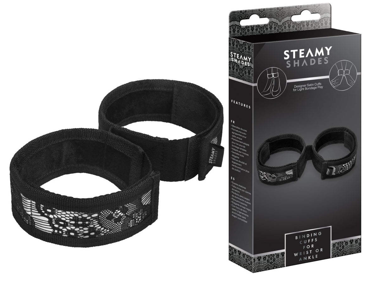 STEAMY SHADES Binding Cuffs gepolsterte Hand- und Fußfesseln in Schwarz mit zwei breiten Manschetten, verstellbaren Verschlüssen und silberfarbenen Verbindungselementen, dargestellt neben der schwarzen Originalverpackung – erhältlich bei Evoria Care