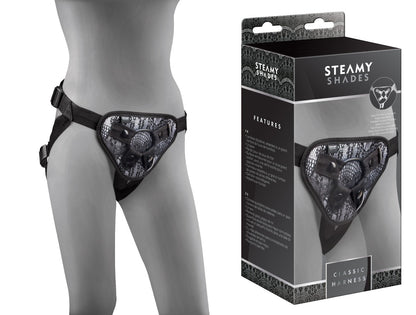 STEAMY SHADES Classic Harness verstellbarer Strap-on Harness in Schwarz mit gemusterter Frontpartie, verstellbaren Hüft- und Schrittgurten sowie zentralem Befestigungsring, an einer grauen Schaufensterpuppe neben der Originalverpackung dargestellt – erhältlich bei Evoria Care