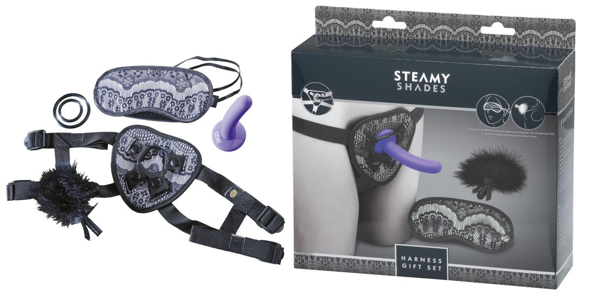 STEAMY SHADES Harness Gift Set mit schwarzem Strap-on Harness, lilafarbenem Dildo, schwarzer Augenmaske und Zubehör, dargestellt neben der schwarz-grauen Originalverpackung – erhältlich bei Evoria Care