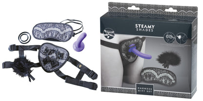 STEAMY SHADES Harness Gift Set mit schwarzem Strap-on Harness, lilafarbenem Dildo, schwarzer Augenmaske und Zubehör, dargestellt neben der schwarz-grauen Originalverpackung – erhältlich bei Evoria Care