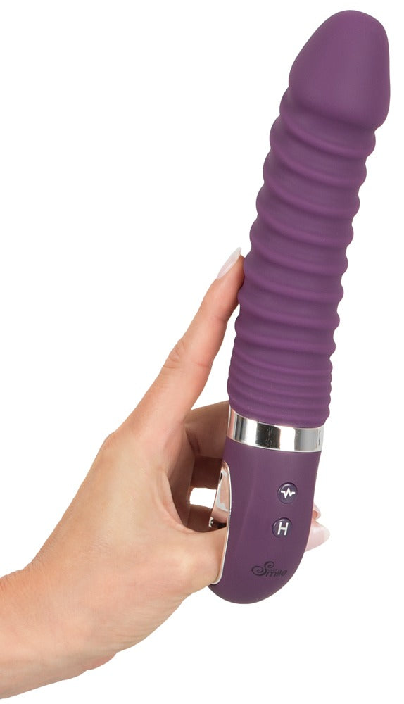 Sweet Smile Warming Soft Wärmevibrator in Dunkelviolett – aufrechte Produktansicht in einer Hand mit strukturiertem Schaft und Haltering – erhältlich bei Evoria Care