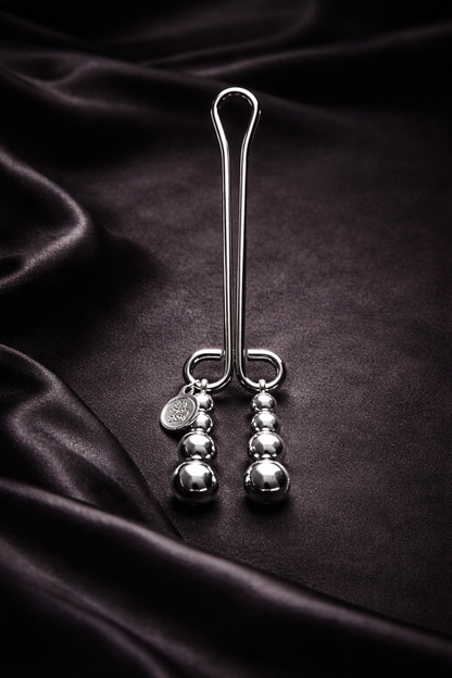 Elegante Klitorisklemme aus Metall mit Kugelketten auf dunklem Stoff inszeniert