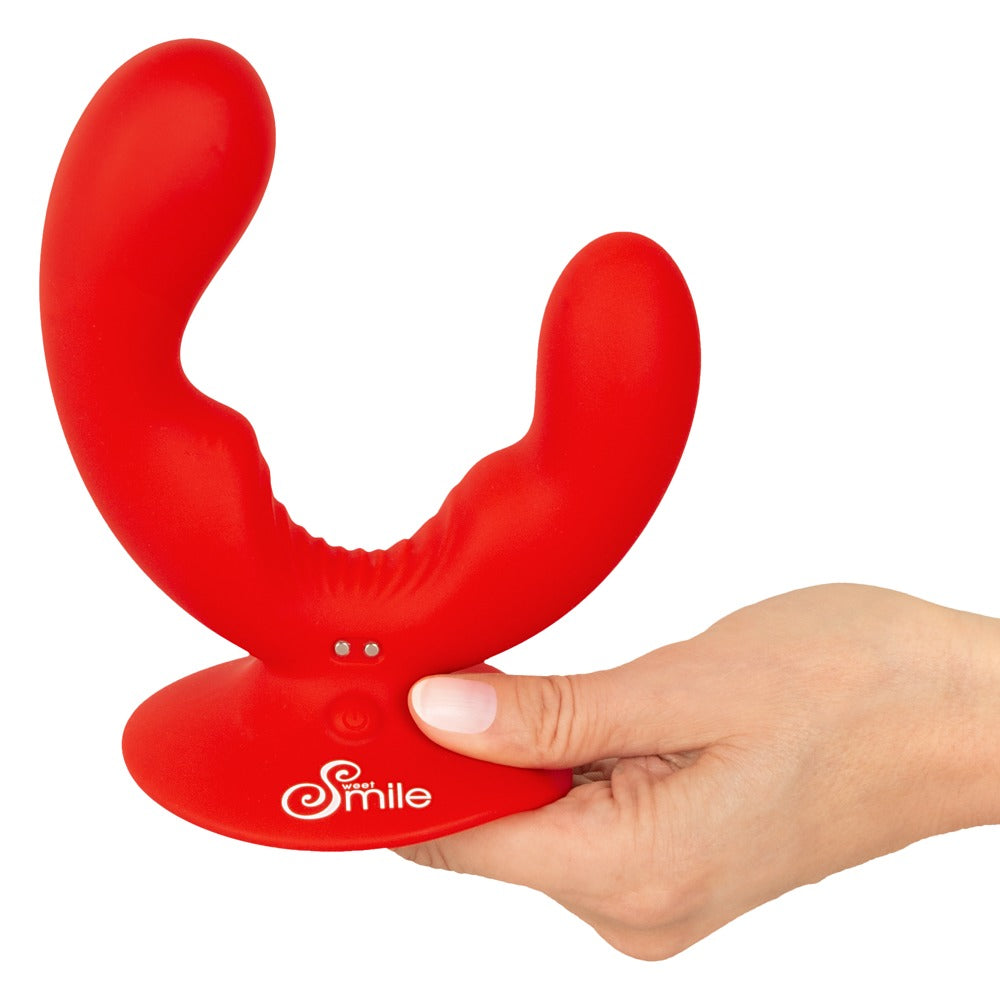 Sweet Smile Doppelvibrator in Rot – Größenvergleich in einer Hand mit zwei gebogenen Stimulationsarmen und Saugfuß