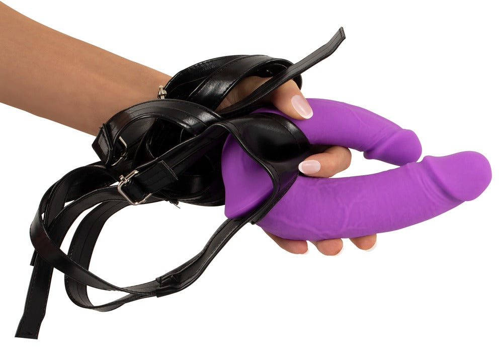 Sweet Smile Super Soft Double Strap-On-Set – Größenvergleich des lilafarbenen Doppeldildos mit schwarzem Harness in einer Hand