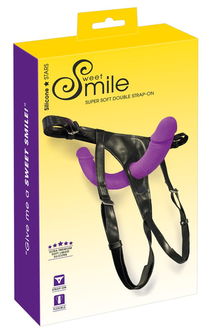 Sweet Smile Super Soft Double Strap-On-Set mit Doppeldildo – schwarzer Harness und lilafarbenes Produkt zusammen mit der gelb-violetten Sweet Smile Verpackung